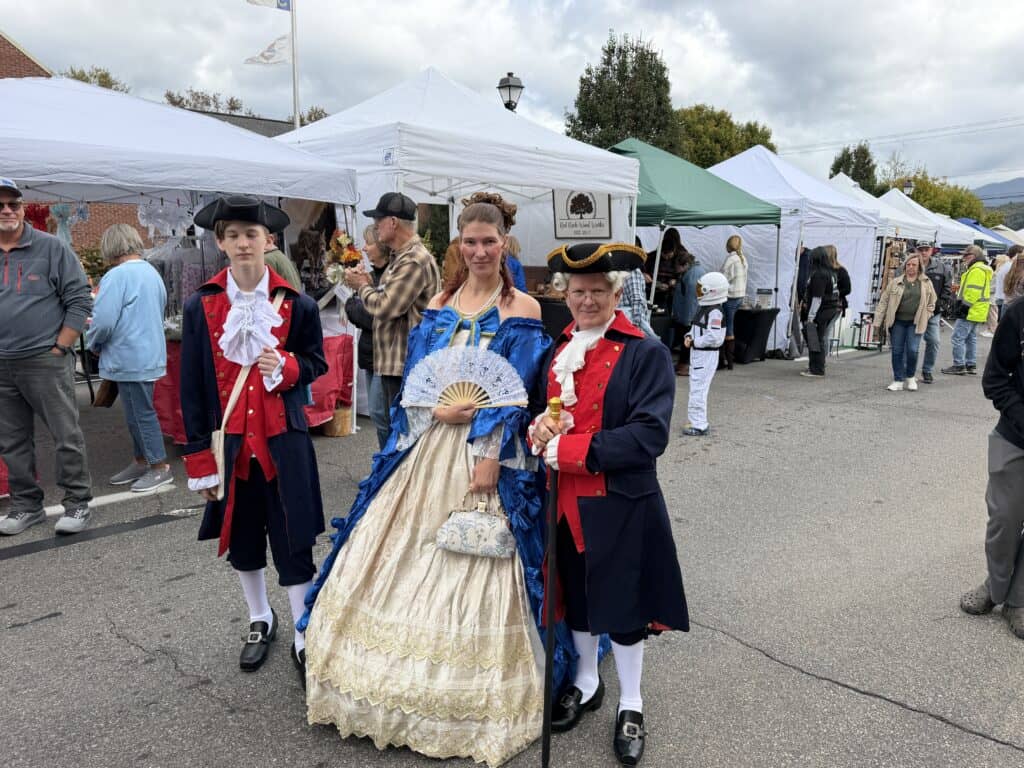 People dressed in historical costumes at Franklin fall festival with tents and crowds.