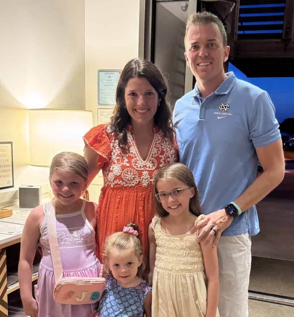 Family portrait with two adults and three children smiling indoors.