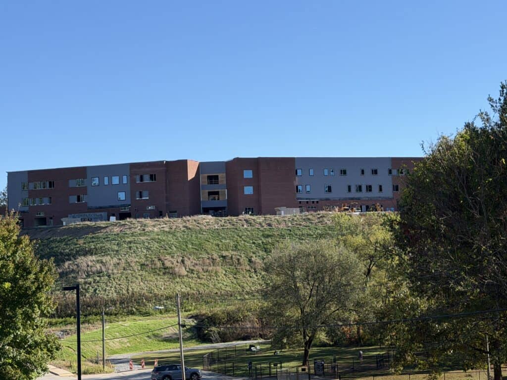 New school building on a hill with trees and a clear blue sky.