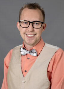 Young male author with glasses and bow tie smiling for the camera.